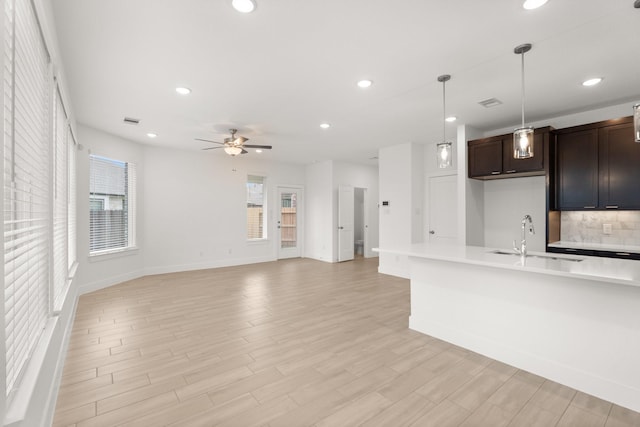 kitchen featuring pendant lighting, sink, backsplash, dark brown cabinets, and light hardwood / wood-style flooring