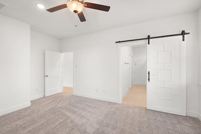 unfurnished bedroom featuring ceiling fan, a barn door, and light carpet