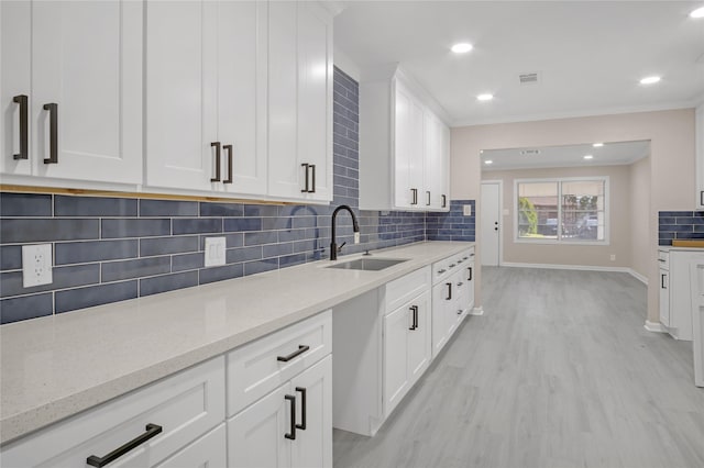 kitchen featuring sink, white cabinets, decorative backsplash, light stone countertops, and light wood-type flooring