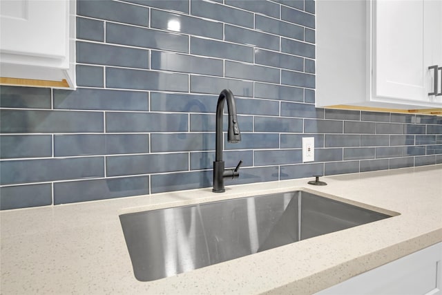 details featuring tasteful backsplash, sink, white cabinetry, and light stone countertops