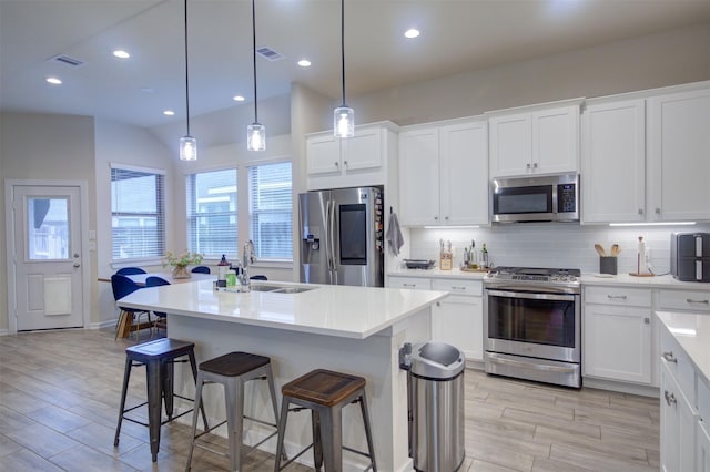 kitchen with appliances with stainless steel finishes, pendant lighting, white cabinetry, an island with sink, and sink