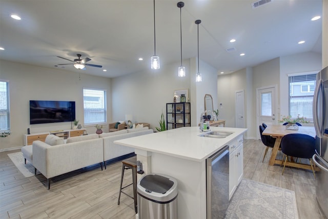 kitchen with pendant lighting, a kitchen island with sink, sink, and light hardwood / wood-style flooring