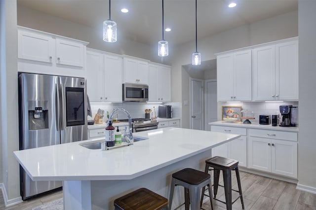 kitchen featuring white cabinetry, appliances with stainless steel finishes, decorative light fixtures, and a center island with sink