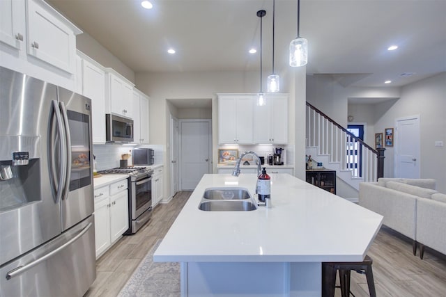 kitchen featuring sink, white cabinetry, stainless steel appliances, a center island with sink, and decorative light fixtures