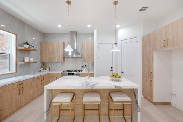 kitchen with a kitchen island with sink, a kitchen breakfast bar, and wall chimney exhaust hood