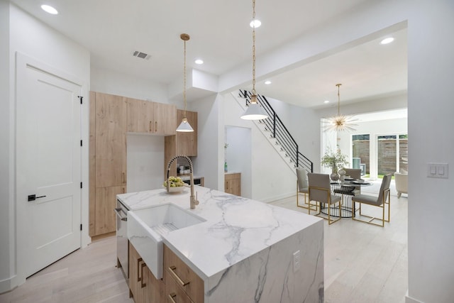 kitchen with light hardwood / wood-style flooring, hanging light fixtures, light stone countertops, an island with sink, and a chandelier