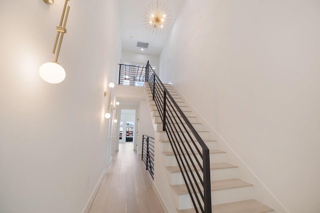 stairway featuring hardwood / wood-style flooring, a towering ceiling, and a chandelier