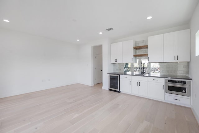 kitchen featuring oven, white cabinets, decorative backsplash, beverage cooler, and light wood-type flooring