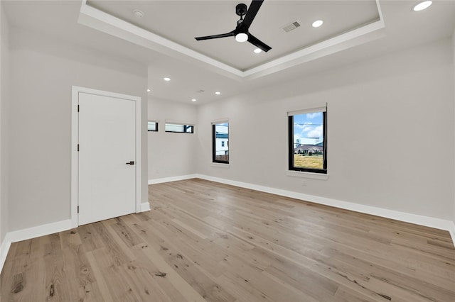 empty room with a tray ceiling, light hardwood / wood-style floors, and ceiling fan