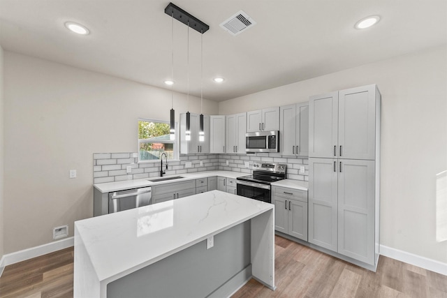 kitchen with a kitchen island, appliances with stainless steel finishes, decorative light fixtures, sink, and gray cabinetry