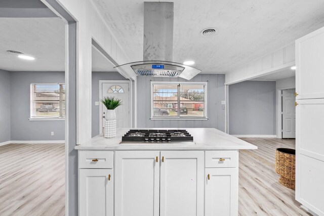 kitchen with light hardwood / wood-style flooring, stainless steel gas cooktop, white cabinets, and island exhaust hood