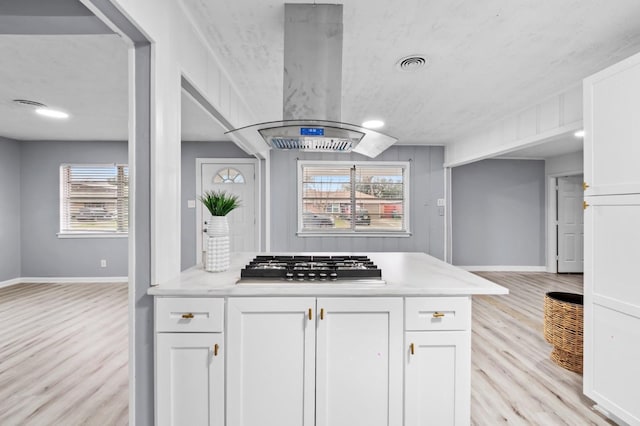 kitchen with island exhaust hood, stainless steel gas cooktop, white cabinets, and light hardwood / wood-style floors