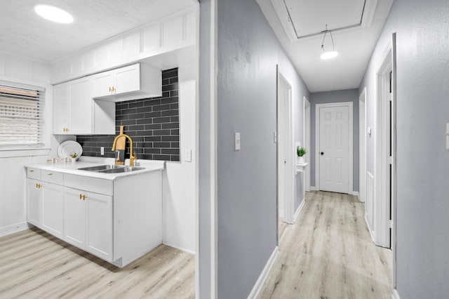 corridor featuring attic access, light wood-type flooring, baseboards, and a sink