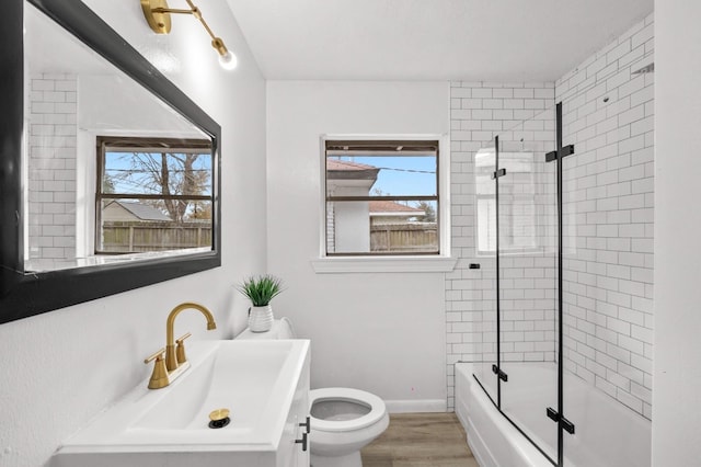 bathroom featuring baseboards, toilet, wood finished floors, enclosed tub / shower combo, and vanity