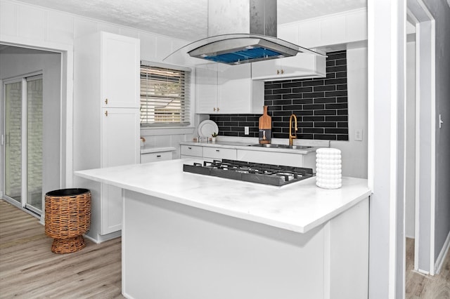 kitchen featuring a sink, light wood-style floors, stainless steel gas stovetop, white cabinets, and island range hood