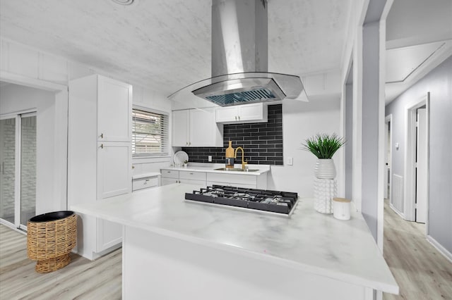 kitchen with island range hood, white cabinetry, light hardwood / wood-style floors, kitchen peninsula, and black gas stovetop