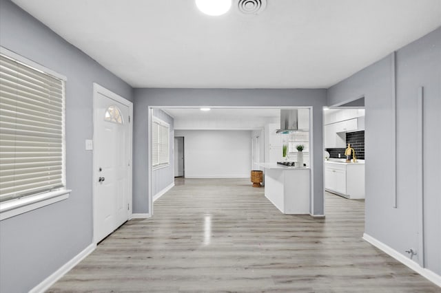 kitchen featuring visible vents, white cabinets, wall chimney exhaust hood, and light wood-style floors