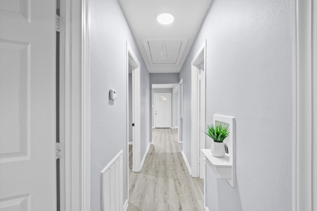 hallway with light wood-type flooring, visible vents, baseboards, and attic access