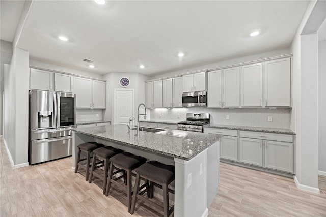 kitchen featuring a kitchen island with sink, appliances with stainless steel finishes, light stone countertops, and sink