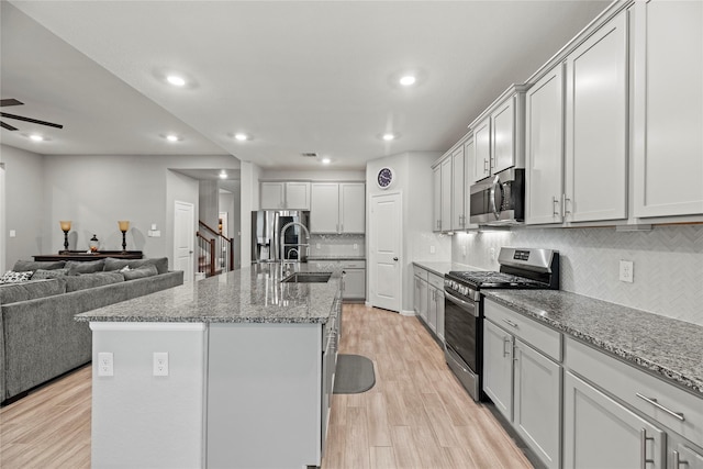 kitchen with sink, appliances with stainless steel finishes, light hardwood / wood-style floors, light stone countertops, and a center island with sink