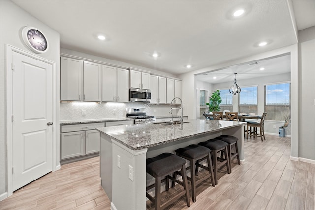 kitchen featuring appliances with stainless steel finishes, stone countertops, sink, gray cabinetry, and a kitchen island with sink