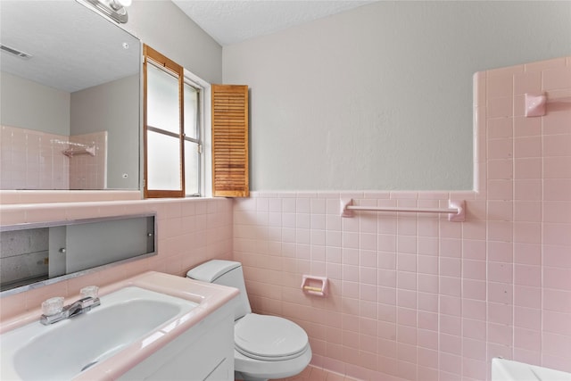 bathroom with tile walls, vanity, walk in shower, toilet, and a textured ceiling