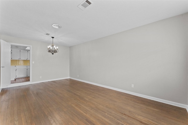 spare room featuring an inviting chandelier and hardwood / wood-style flooring