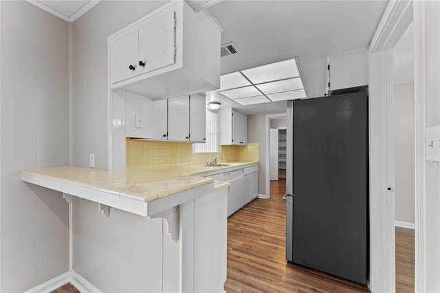 kitchen with hardwood / wood-style floors, white cabinets, stainless steel fridge, a kitchen breakfast bar, and tile counters