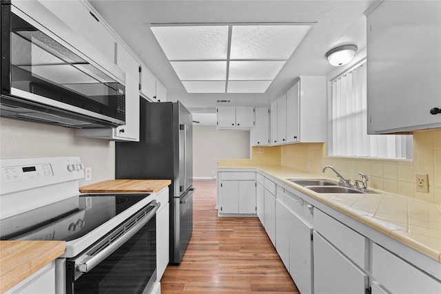 kitchen with appliances with stainless steel finishes, tasteful backsplash, sink, white cabinets, and light hardwood / wood-style floors