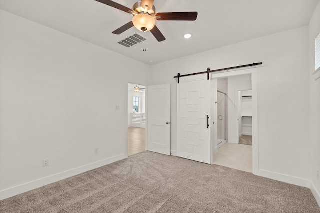 unfurnished bedroom with a barn door, light carpet, and ceiling fan