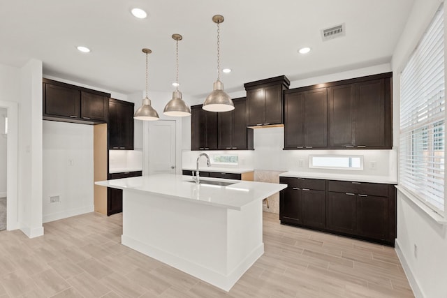 kitchen with dark brown cabinets, sink, a kitchen island with sink, and hanging light fixtures