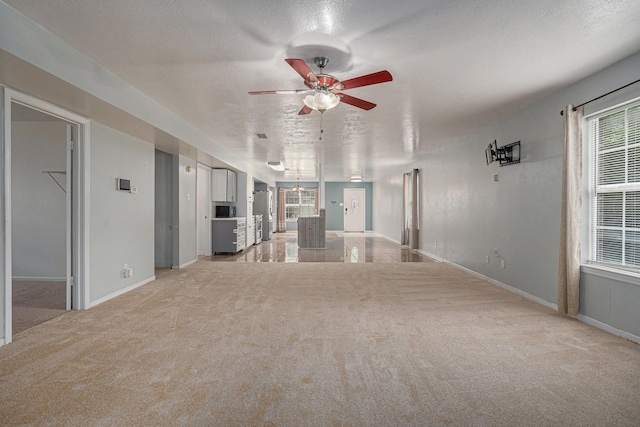 unfurnished living room with ceiling fan, light colored carpet, and a textured ceiling