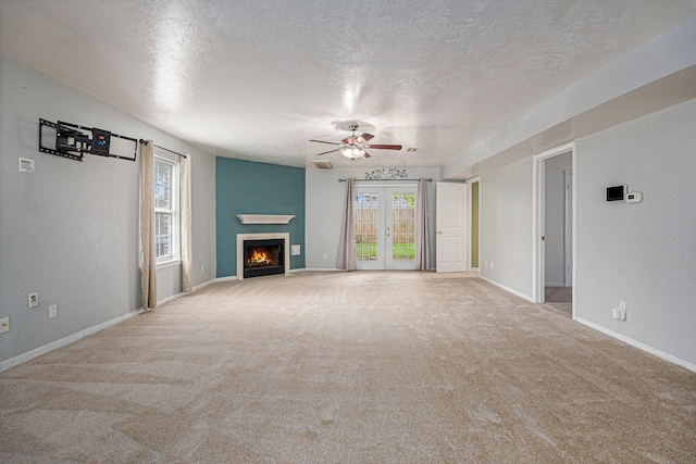 unfurnished living room with ceiling fan, light colored carpet, a textured ceiling, and french doors