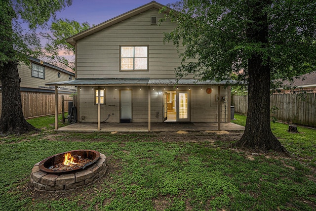 back house at dusk with an outdoor fire pit, a patio, and a lawn