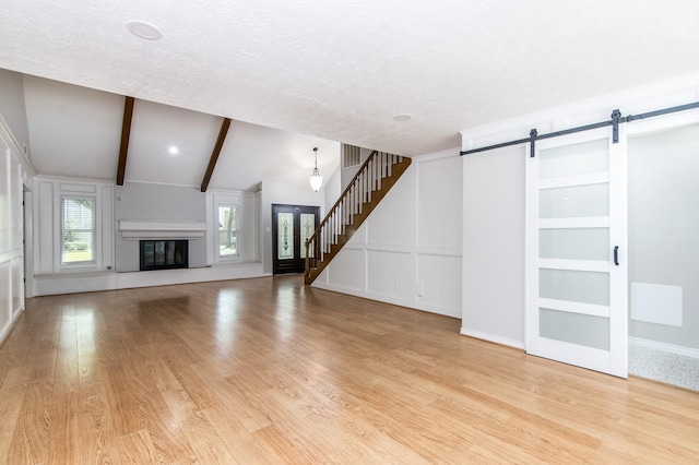 unfurnished living room with a barn door, light hardwood / wood-style floors, a textured ceiling, and vaulted ceiling with beams