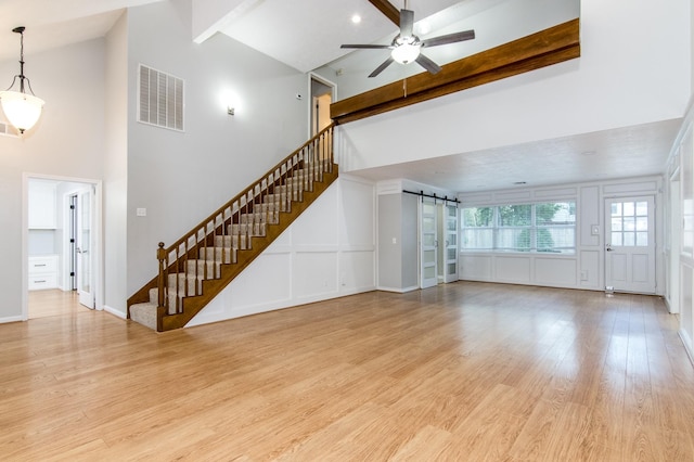 unfurnished living room with ceiling fan, high vaulted ceiling, light hardwood / wood-style floors, a barn door, and beamed ceiling