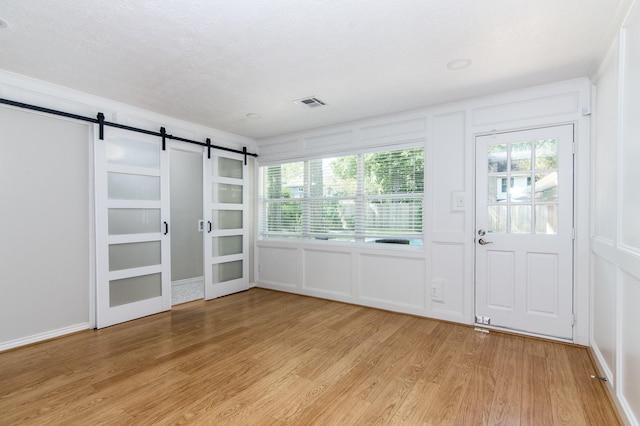 interior space with a barn door, a textured ceiling, and light hardwood / wood-style flooring