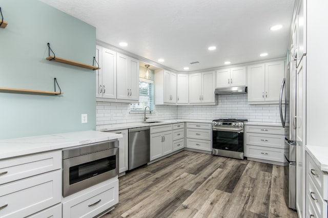 kitchen with sink, appliances with stainless steel finishes, white cabinetry, backsplash, and dark hardwood / wood-style flooring