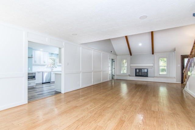 unfurnished living room featuring vaulted ceiling with beams, light hardwood / wood-style flooring, and sink