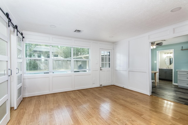 spare room with ceiling fan, light hardwood / wood-style floors, a barn door, and a textured ceiling