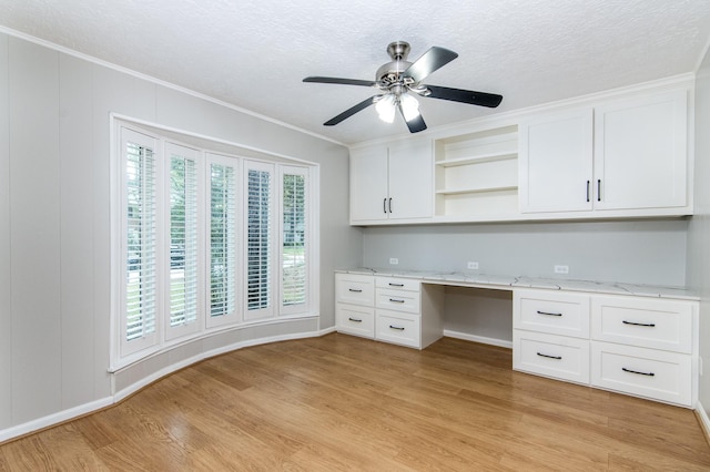 unfurnished office featuring ceiling fan, ornamental molding, built in desk, and light hardwood / wood-style floors