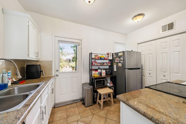 kitchen featuring light tile patterned flooring, sink, tasteful backsplash, stainless steel fridge, and white cabinets