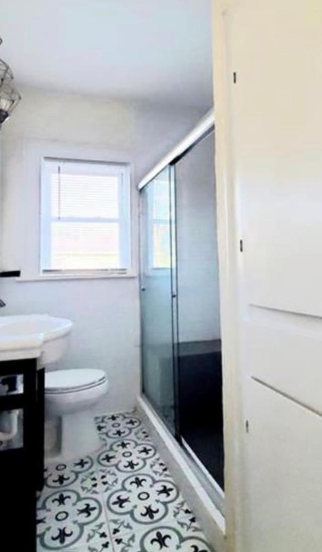 bathroom featuring tile patterned floors, toilet, and a shower with shower door