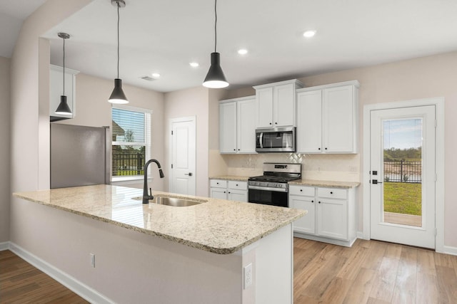 kitchen featuring sink, pendant lighting, stainless steel appliances, light stone countertops, and white cabinets