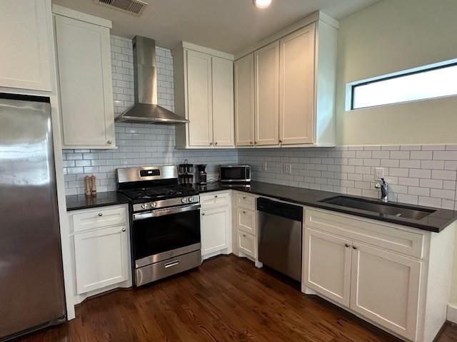 kitchen with appliances with stainless steel finishes, white cabinetry, sink, decorative backsplash, and wall chimney range hood