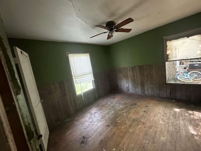 spare room featuring wood-type flooring, wooden walls, and ceiling fan