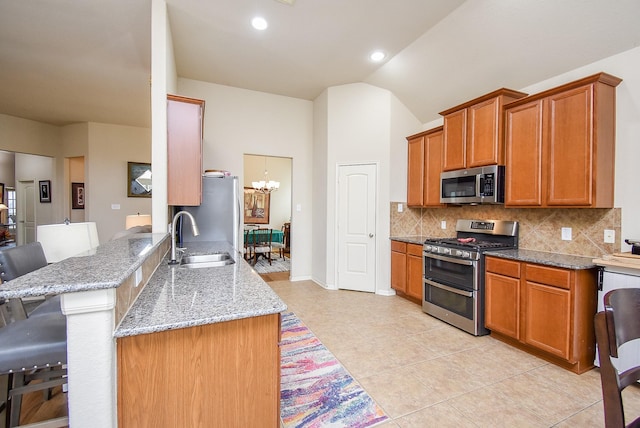 kitchen featuring sink, a breakfast bar, stainless steel appliances, light stone counters, and kitchen peninsula