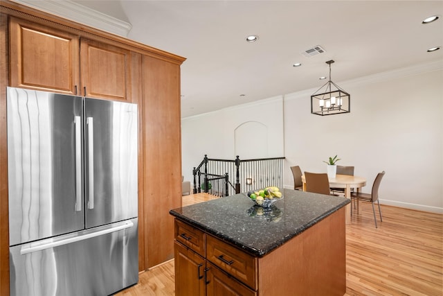 kitchen with crown molding, light wood-type flooring, stainless steel fridge, a kitchen island, and dark stone counters