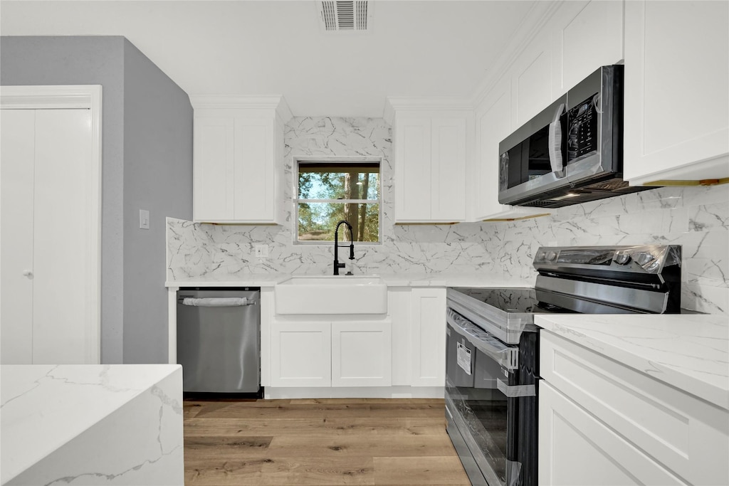 kitchen with light stone counters, white cabinetry, appliances with stainless steel finishes, and sink