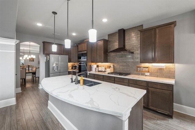 kitchen featuring pendant lighting, sink, appliances with stainless steel finishes, an island with sink, and wall chimney exhaust hood